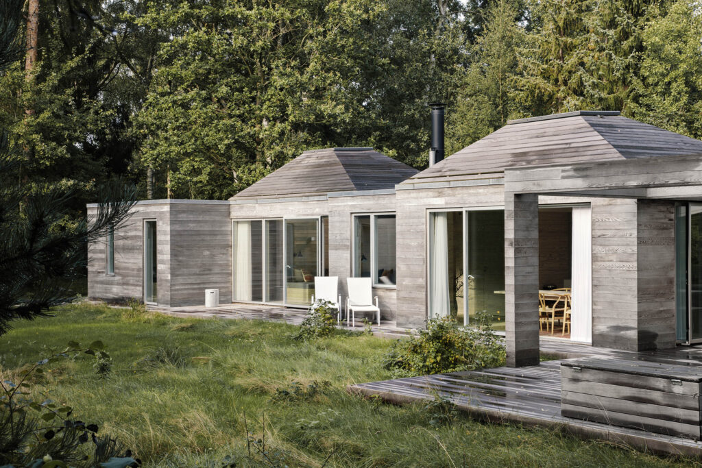 Sommerhus med træbeklædning og terrasse omgivet af træer.