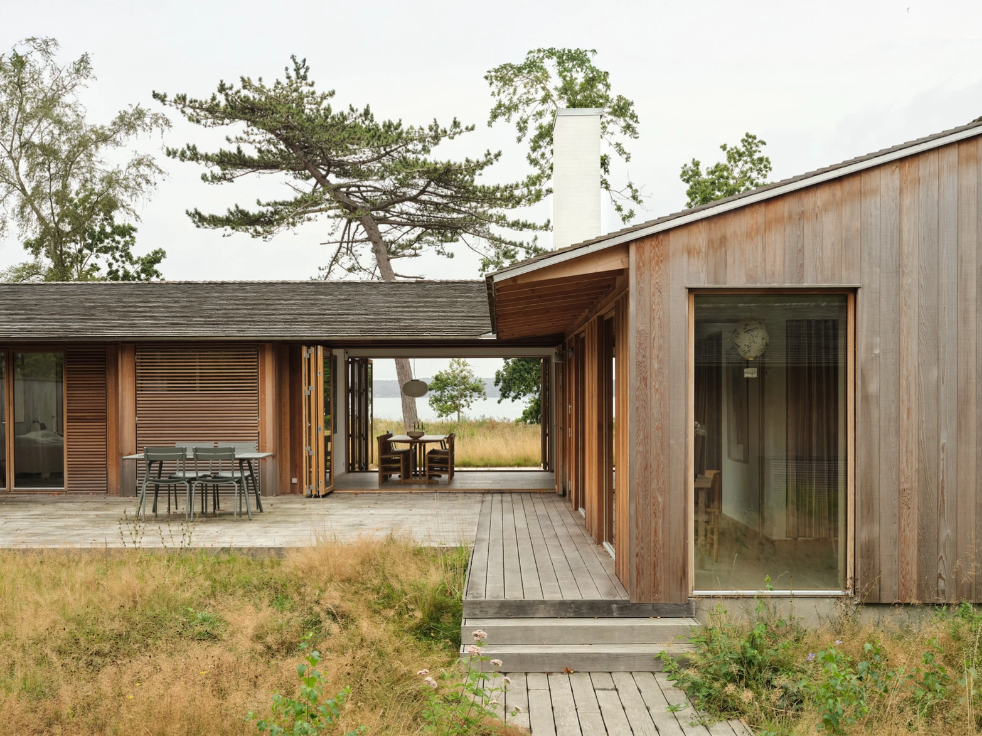 Træbeklædt hus med overdækket terrasse og store vinduer.