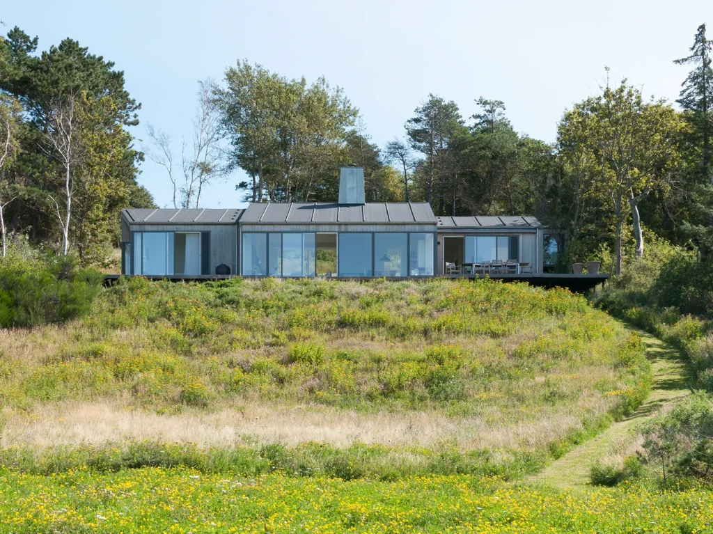 Langstrakt hus med store vinduer ud mod en grøn græsplæne.