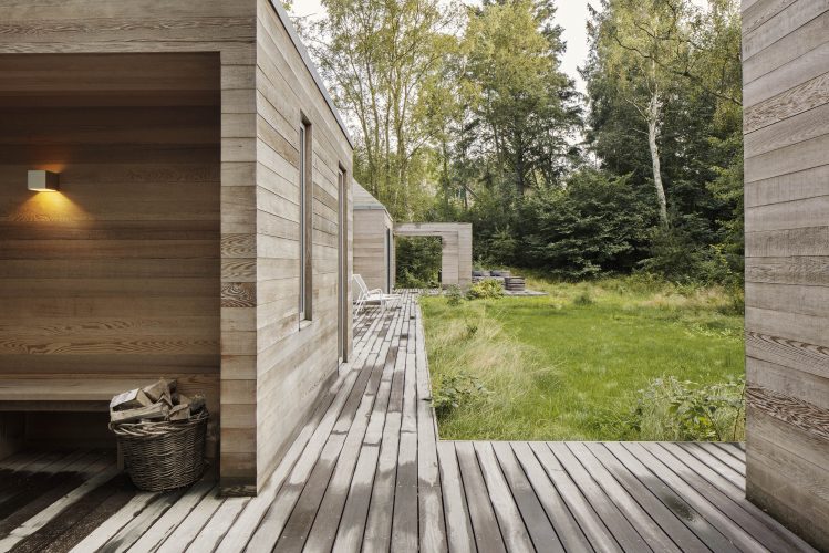 Træterrasse langs et sommerhus med udsigt til haven.